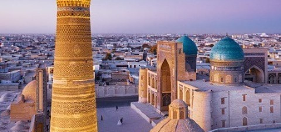 Colorful sunset twilight over the famous Old Town in the City of Bukhara with the iconic Kalyan Minaret and Miri Arab Madressa. Aerial Drone Point of View. Itchan Kala, Bukhara, Khorezm Region, Uzbekistan, Central Asia.